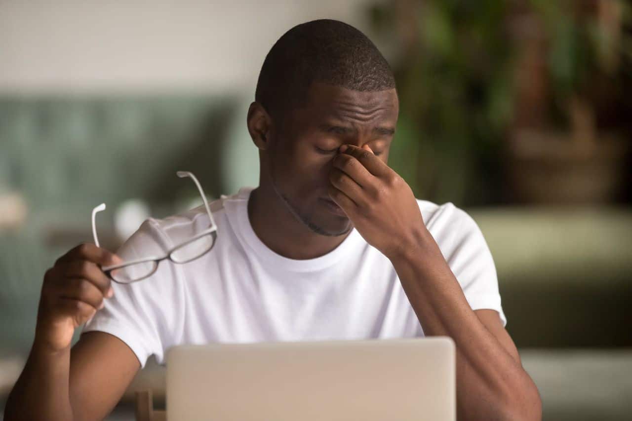 Man rubs his dry eyes while sitting in front of a computer