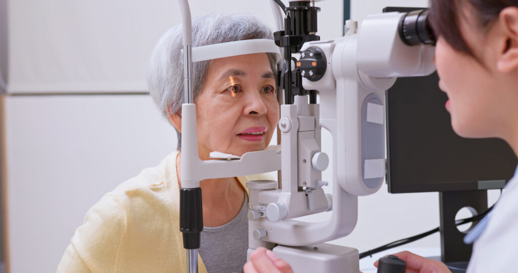 Older woman undergoing a slit-lamp eye exam for cloudy vision after cataract surgery.